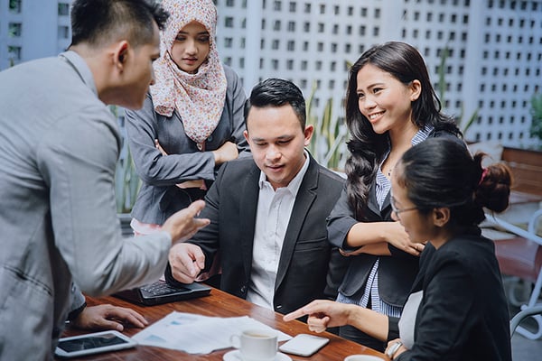 A group of coworkers in business attire collaborating at a restaurant table outdoors.