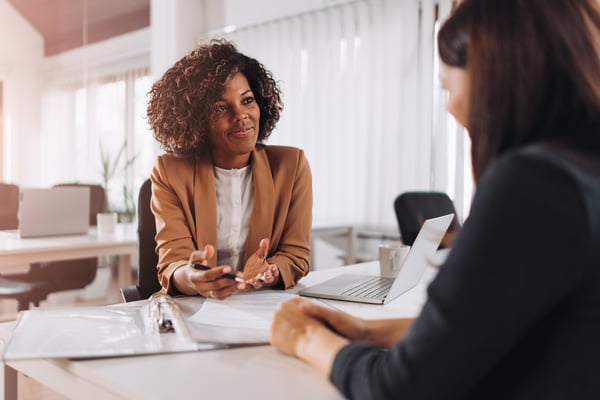 A Right Management coach sits at a table in an office with her laptop open, providing career development coaching to an Operation HOPE client. This session is part of their collaborative initiative aimed at empowering individuals and communities nationwide. 