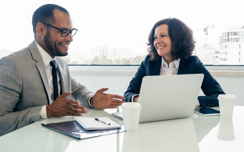 Two professionals in an office discuss career development programs while working on a laptop, with notebooks on the table   Professionals collaborating on career development programs in a modern workplace environment 