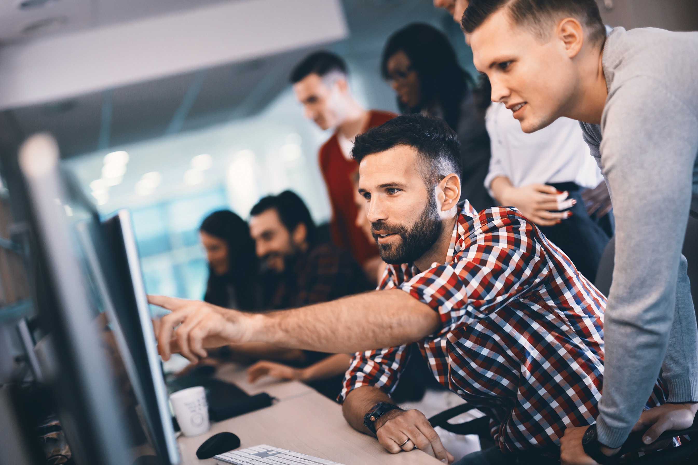 A group of coworkers collaborating in front of a computer screen as one of the team members points to the screen.